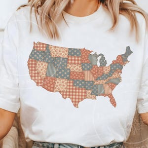May include: White t-shirt featuring a patchwork design of the United States map. The map is composed of various patterns in red, blue, and beige, including stars, stripes, and floral prints. The shirt is a casual, everyday wear item.
