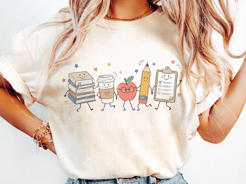 Peut inclure: Un t-shirt couleur cr&egrave;me arborant une impression graphique de cinq fournitures scolaires anthropomorphes se tenant par la main. Les personnages incluent une pile de livres, un gobelet &agrave; caf&eacute;, une pomme &agrave; lunettes, un crayon jaune et un presse-papiers.