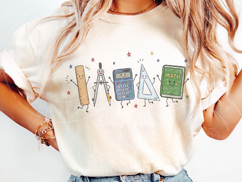 Puede incluir: Una camiseta de color crema con un estampado gr&aacute;fico de cinco &uacute;tiles escolares antropom&oacute;rficos: una regla, un comp&aacute;s, una calculadora, una escuadra y un libro verde con la etiqueta "MATH" con caras sonrientes, rodeados de peque&ntilde;as estrellas coloridas.