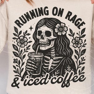 May include: Beige sweatshirt with a black and white graphic. The graphic shows a skeleton with long hair, a flower, and a coffee cup. Text reads "RUNNING ON RAGE & iced coffee."