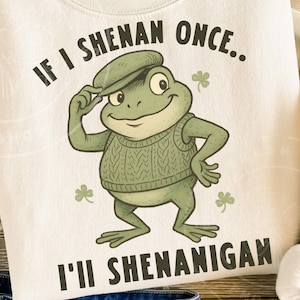 May include: Cream-colored sweatshirt featuring a cartoon frog wearing a green sweater vest and cap. The text "IF I SHENAN ONCE.. I'LL SHENANIGAN" is printed in black. Shamrock graphics are also included.