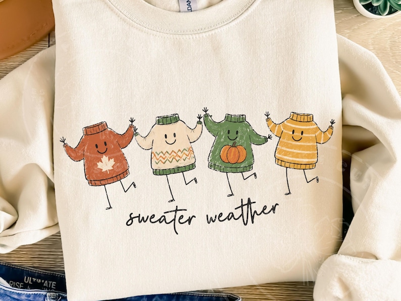 May include: A cream-coloured sweatshirt with a playful design of four animated sweaters in autumnal hues: rust, cream, green, and yellow. Each sweater has a smiling face and is dancing. The words "sweater weather" are written in a script font below.
