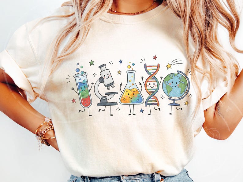 Puede incluir: Una camiseta de color crema con un estampado gr&aacute;fico colorido de equipos cient&iacute;ficos animados que incluyen un tubo de ensayo, un microscopio, un matraz, una cadena de ADN y un globo terr&aacute;queo, todos con caras sonrientes y peque&ntilde;as estrellas.