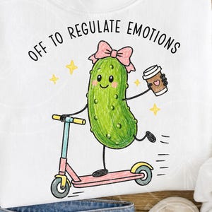 May include: A white sweatshirt featuring a graphic of a green pickle character wearing a pink bow, riding a pink and blue scooter while holding a coffee cup. The text above the character reads OFF TO REGULATE EMOTIONS in black capital letters.