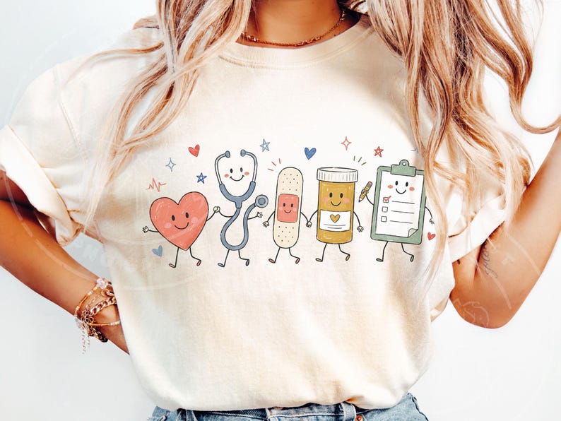 May include: A cream-colored t-shirt featuring a graphic print of five anthropomorphic medical items holding hands: a red heart, a blue stethoscope, a tan adhesive bandage, a yellow pill bottle, and a green clipboard with a checklist.