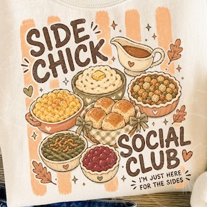 May include: Cream-coloured sweatshirt with a graphic featuring various Thanksgiving side dishes. Text includes "SIDE CHICK SOCIAL CLUB" and "I'M JUST HERE FOR THE SIDES". The design incorporates autumnal colours and decorative elements.