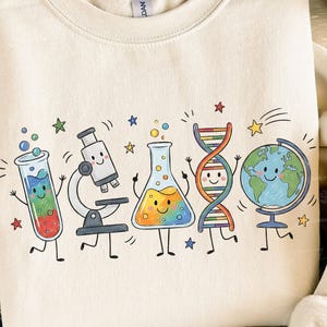 Puede incluir: Una sudadera de cuello redondo color crema con un estampado gr&aacute;fico colorido de cinco iconos cient&iacute;ficos antropom&oacute;rficos: un tubo de ensayo, un microscopio, un matraz Erlenmeyer, una doble h&eacute;lice de ADN y un globo terr&aacute;queo, todos con caras sonrientes.