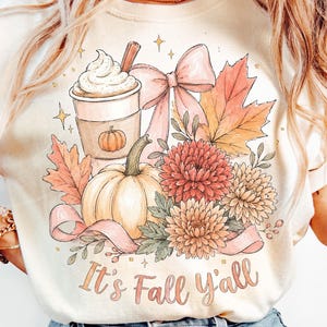 May include: Cream-colored sweatshirt featuring a fall-themed graphic. The design includes a pumpkin spice latte, pumpkin, fall leaves, flowers, and a bow. The text "It's Fall y'all" is written in a script font.