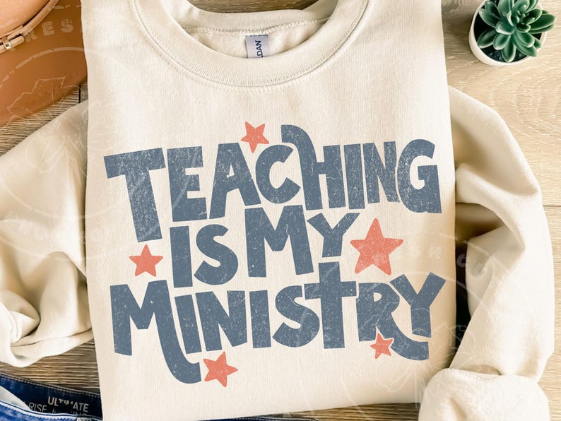 May include: Cream-colored sweatshirt with the text "TEACHING IS MY MINISTRY" in distressed blue lettering. Red stars accent the text. A casual, comfortable top for teachers.