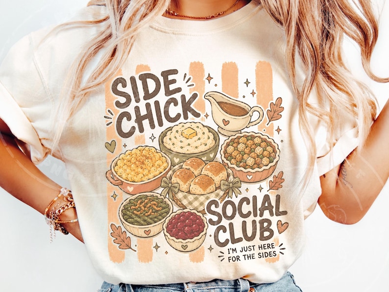 May include: Cream-coloured t-shirt with a graphic featuring various Thanksgiving side dishes and the text "SIDE CHICK SOCIAL CLUB". The design includes a gravy boat, mashed potatoes, stuffing, rolls, and other dishes.