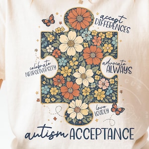 May include: Cream-colored t-shirt featuring a floral puzzle piece design with the words "accept differences," "advocate always," "love loudly," and "autism acceptance." The puzzle piece is filled with flowers in shades of orange, yellow, and blue, with butterflies.