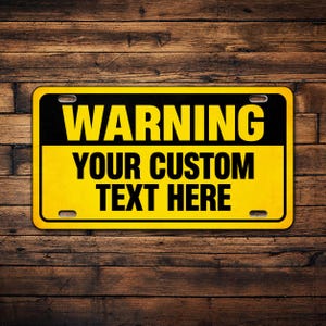 May include: A rectangular metal sign with rounded corners and four mounting holes. The top section features a black background with the word WARNING in bold yellow text. The bottom section has a yellow background with the black text YOUR CUSTOM TEXT HERE.