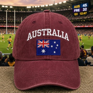 May include: A maroon baseball cap featuring the word AUSTRALIA embroidered in white arched text above a rectangular patch of the Australian flag, which displays the Union Jack and white stars on a blue background, centered on the front panel.