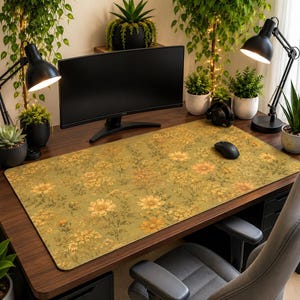 May include: A rectangular desk mat featuring a repeating floral pattern with yellow and orange flowers on a muted olive green background. The mat is positioned on a dark wood desk surface, providing a flat area for computer peripherals.