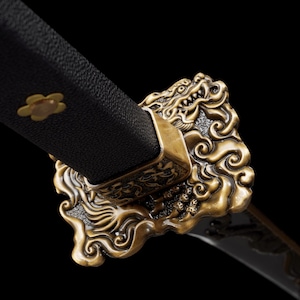 May include: Close-up of a katana sword hilt. The black handle is adorned with a gold flower emblem. The guard features an ornate, gold dragon design. The blade is visible, with a dark finish.