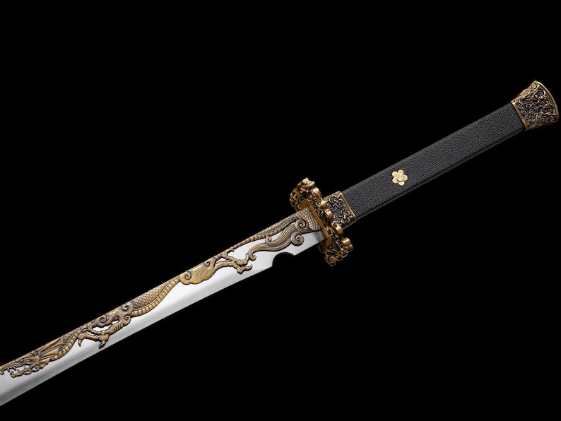 May include: A detailed close-up of a decorative sword with a silver blade and ornate gold-colored handle and guard. The blade features a dragon design. The handle is black with a gold flower emblem. The sword is set against a black background.