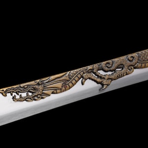May include: Close-up of a decorative sword blade with a detailed bronze dragon design. The dragon's head and claws are prominently featured on the hilt, with a silver blade extending from the dragon's mouth.