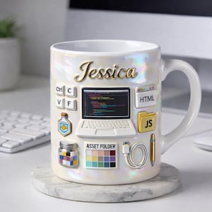 Könnte beinhalten: Weißer Keramikbecher mit schillerndem Finish und dem Namen "Jessica" in goldener Schrift. Der Becher ist mit computerbezogenen Symbolen wie einem Laptop, Tastaturtasten und HTML- und JS-Symbolen verziert. Der Becher steht auf einem Marmoruntersetzer.