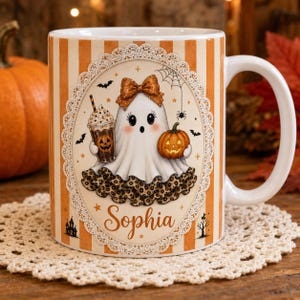 May include: A white ceramic mug with orange and white vertical stripes featuring a central oval illustration of a ghost wearing a brown bow, holding a pumpkin and a coffee cup, with the name Sophia printed below in a script font.