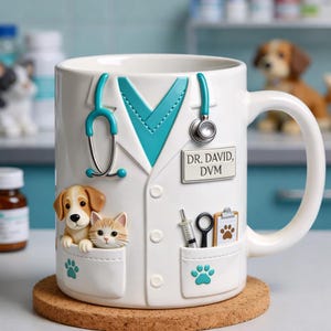 Può includere: Tazza in ceramica bianca progettata come un camice da veterinario, con colletto e stetoscopio turchese. La tazza ha tasche con un cucciolo e un gattino, una siringa e un blocco per appunti. Il testo "DR. DAVID, DVM" è presente.