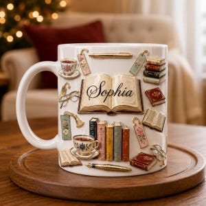 May include: A white ceramic mug featuring a raised, three-dimensional design of an open book with the name Sophia printed in black script. The mug is decorated with colorful illustrations of stacked books, teacups, bookmarks, and fountain pens.