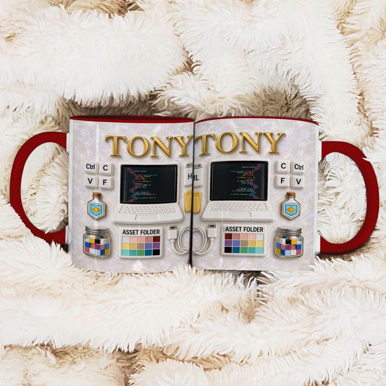 Może przedstawiać: Dwa białe ceramiczne kubki z czerwonymi uchwytami i obw&oacute;dkami. Każdy kubek ma złoty napis "TONYTONY". Kubki są ozdobione grafiką laptop&oacute;w, fragmentami kodu i słowami "ASSET FOLDER".