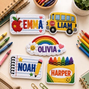 May include: Five embroidered patches featuring school-themed designs and names. One patch is a notebook page with an apple and 'EMMA', a yellow school bus with 'LIAM', a rainbow with a flower and 'OLIVIA', a notebook with 'NOAH', and a crayon box with 'HARPER'.