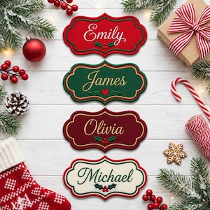 May include: Four decorative scalloped-edge name plaques featuring embroidered text. The top plaque is red with white text reading Emily, the second is green with gold text reading James, the third is dark red with gold text reading Olivia, and the bottom is cream with green text reading Michael.