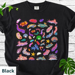 May include: Black t-shirt featuring a colorful illustration of various sea slugs. The design includes a variety of shapes and colors, including red, yellow, blue, and purple. The text "Black" is at the bottom left.