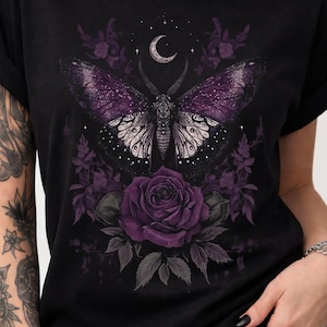 May include: Black t-shirt featuring a detailed graphic of a moth with purple wings, a crescent moon, and a large purple rose. The design includes floral elements and stars, creating a gothic or fantasy aesthetic.