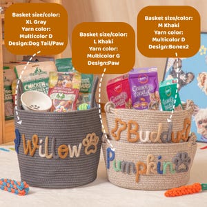 May include: Three woven pet baskets in grey and khaki, filled with treats and toys. The grey basket has "Willow" and a paw print, the khaki baskets have "Buddah" and "Pumpkin" with bone and paw designs. The baskets are labelled with size, colour, and design details.