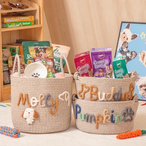May include: Three beige rope baskets filled with pet supplies. The largest basket is labelled "Molly" with a dog applique. The other baskets are labelled "Buddy" and "Pumpkin" with a paw print. The baskets contain pet food, a bowl, and toys.