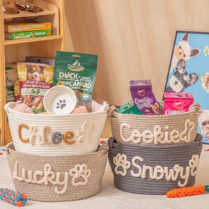 May include: Four woven rope pet baskets, stacked. The top basket is white with "Chloe" and a cat silhouette. The next basket is tan with "Lucky" and a paw print. The other two baskets are tan and grey with pet names.