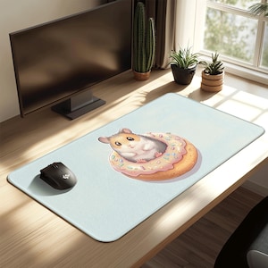 May include: A light blue rectangular mousepad featuring a cartoon hamster inside a donut with pink frosting and sprinkles. A black computer mouse is on the left. The mousepad is on a wooden desk.