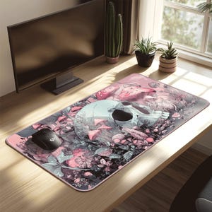 May include: A rectangular mouse mat with a detailed illustration of a skull surrounded by mushrooms and foliage in shades of pink, grey, and green. A black computer mouse is on the left side of the mat.
