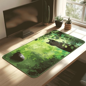 Puede incluir: Alfombrilla de ratón rectangular verde con una ilustración de un gato negro sobre un fondo verde frondoso. Un ratón de ordenador negro está situado a la izquierda. La alfombrilla está sobre un escritorio de madera cerca de un monitor de ordenador.