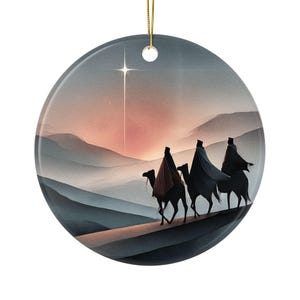 Op de afbeelding: Ronde keramische kerstversiering met een artistieke afbeelding van de Drie Wijzen op kamelen, tegen een achtergrond van een zonsondergang en een heldere ster. Het ornament heeft een gouden ophangkoord.