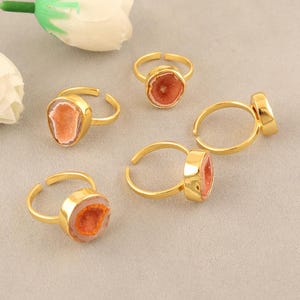 May include: Five gold-toned rings featuring circular settings with textured, peach-colored druzy stone centers. Each ring has a thin, adjustable metal band. The stones exhibit a crystalline, sparkling surface texture within a smooth gold-colored bezel.
