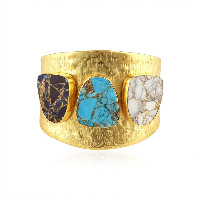May include: A wide gold-tone cuff bracelet featuring three inlaid stones. The stones are a dark blue with gold flecks, turquoise, and white with gold veining. The bracelet has a textured surface.