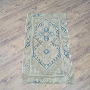 Könnte beinhalten: Rechteckiger Teppich im Vintage-Stil mit einem zentralen geometrischen Design in Blau- und Beigetönen. Der Teppich hat einen Rand mit sich wiederholenden Mustern und liegt auf einem Holzboden.