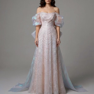 Puede incluir: Un vestido largo hasta el suelo, con hombros descubiertos en tono rosa pálido, con intrincados bordados de lentejuelas plateadas en patrón de remolinos. Incluye mangas abullonadas de organza iridiscente y una cola transparente.