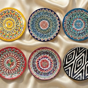 以下が含まれることがあります： 黒いハンドルと「But First, Coffee」のテキストが黒い太字で書かれた白いセラミックマグ。マグは白い表面に置かれています。マグの高さは10cmです。