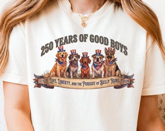May include: Ivory-colored t-shirt featuring a graphic of six dogs wearing patriotic hats and bandanas. The text reads "250 YEARS OF GOOD BOYS" above the dogs and "LIFE, LIBERTY, AND THE PURSUIT OF BELLY RUBS" below. The shirt has a relaxed fit.