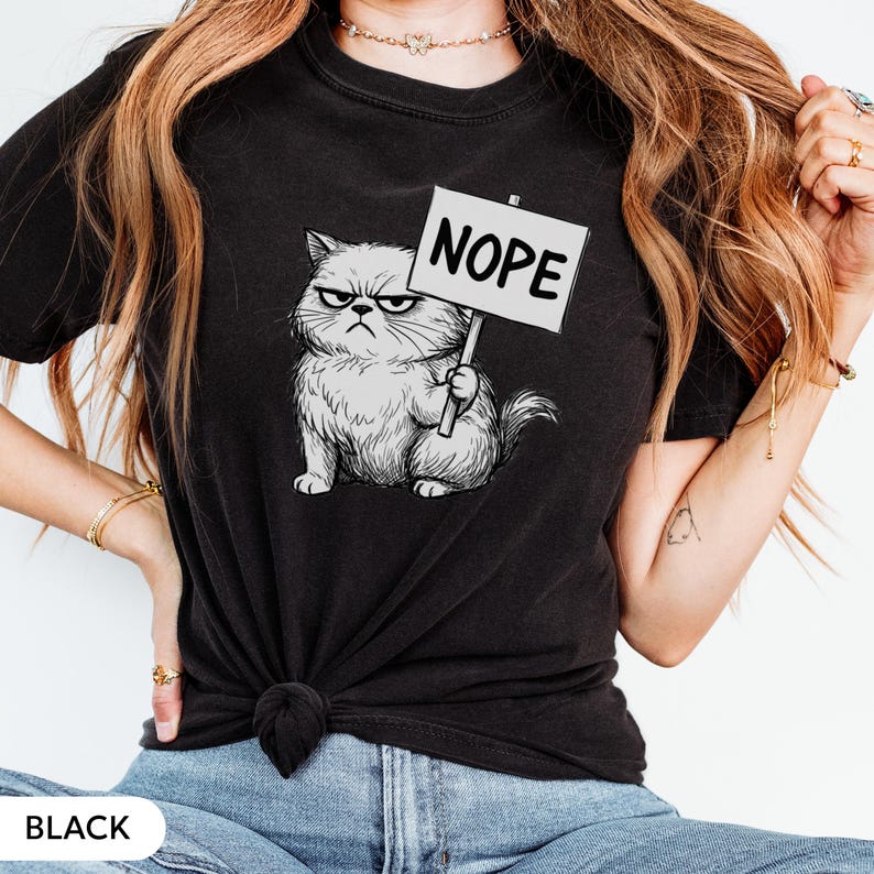 Może przedstawiać: Czarny t-shirt z rysunkiem wściekłego kota trzymającego znak z napisem "Nope". Kot jest szary i biały, z ponurym wyrazem twarzy. Rysunek jest szczeg&oacute;łowy i zacieniony.