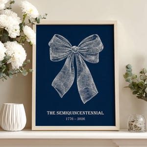 May include: A framed print featuring a detailed white bow illustration on a navy blue background. The text "THE SEMIQUINCENTENNIAL 1776 - 2026" is displayed below the bow. The artwork is displayed on a white mantelpiece with floral arrangements.