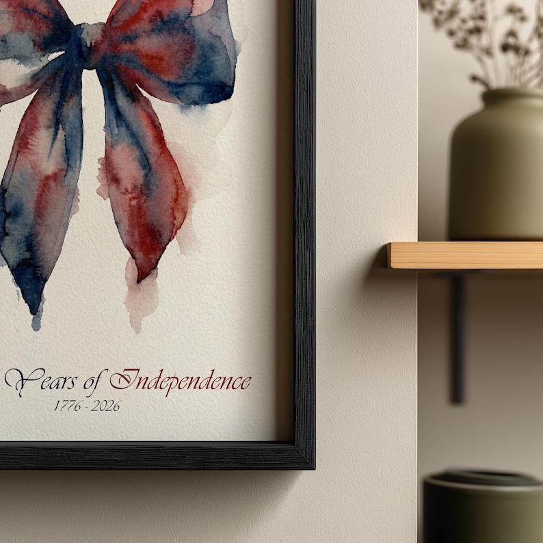 May include: Watercolor print of a bow in shades of red and blue, framed in black. The artwork is titled "Years of Independence" with the dates 1776-2026 in a decorative font. The bow is painted with watercolor techniques.