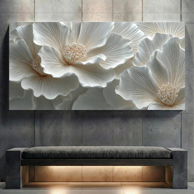 May include: A large, rectangular wall art piece featuring a close-up of white, textured flowers with detailed petals and beige centers. The artwork is mounted on a gray concrete wall above a bench with a gray cushion and a wooden frame.