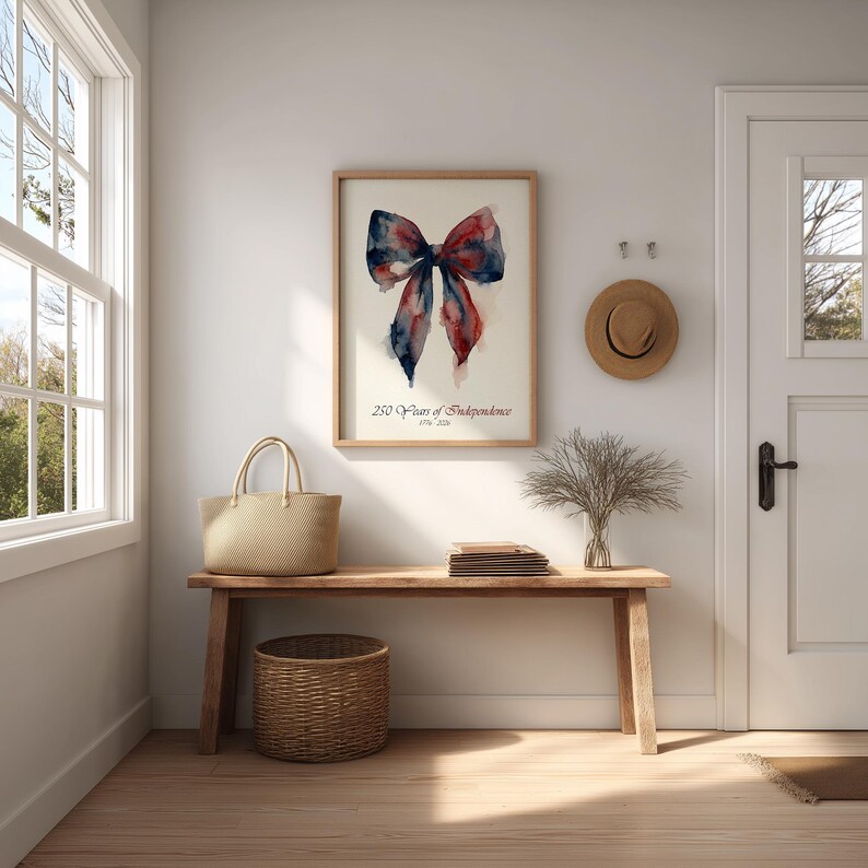 May include: A framed watercolor print featuring a bow in shades of red, white, and blue, with the text "250 Years of Independence 1776-2026." The print hangs above a wooden bench with a woven basket and tote bag.