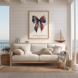 May include: A framed watercolor print featuring a bow in shades of red and blue. The print is displayed above a white sofa in a bright, airy room. The text "250 Years of Independence 1776-2026" is below the bow.