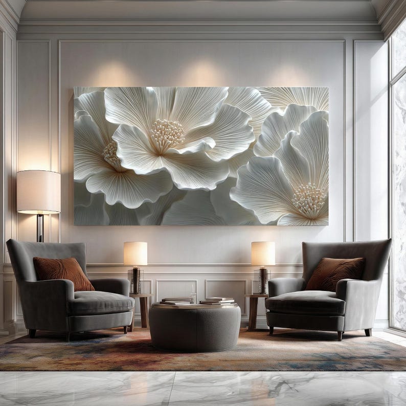 May include: A large, rectangular wall art piece featuring a detailed, textured relief of white flowers. The artwork is the focal point of a room with two gray armchairs, lamps, and a round ottoman. The room has a modern, elegant aesthetic.